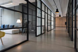 A modern office building with glass office doors and walls and lights down the hallway
